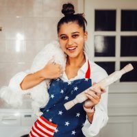 Cheerful woman with a rolling pin holding a cute white Maltese dog in the kitchen
